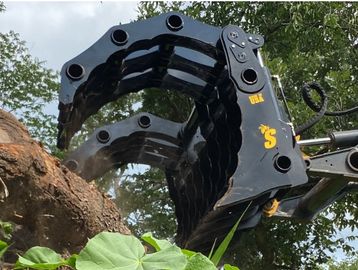 Heavy machinery claw gripping a large tree trunk outdoors.