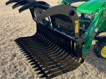 A green tractor with a large black Stinger attachment on dry grass.