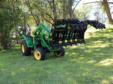 Green tractor with a large front loader attachment on a grassy field.