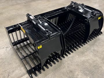 A large, black grapple bucket attachment for heavy machinery on a concrete floor.