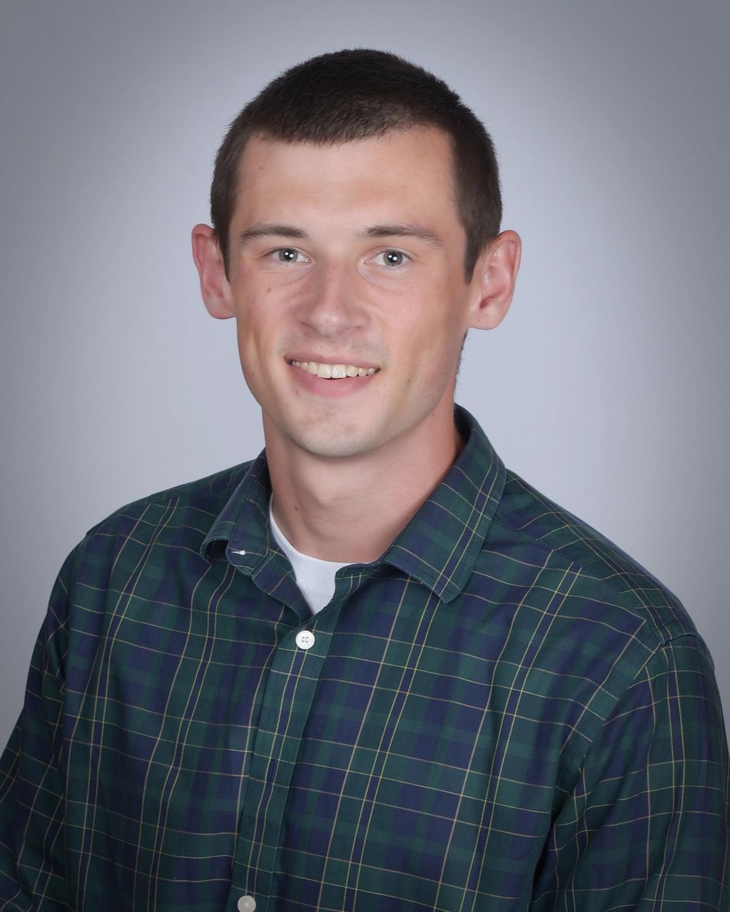 Young man smiling in plaid shirt.