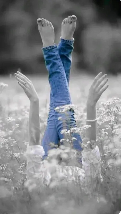 A black and white image of legs crossed in a field of flowers the only color is the blue jeans.