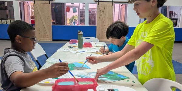 Three boys painting together at a table in a bright, spacious room.