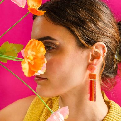 Woman with orange floral earrings and flowers against a pink background.