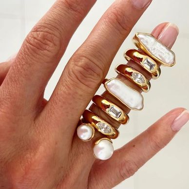 Unique multi-band gold ring with pearls and gemstones on a hand.