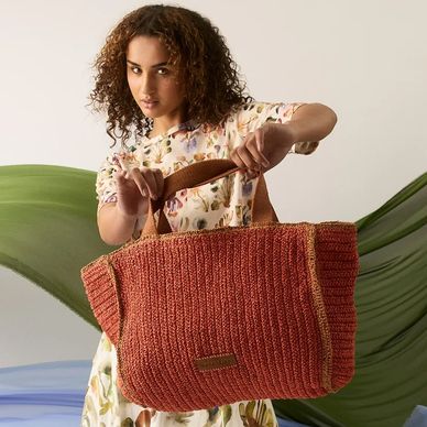 Woman holding a large knitted rust-colored bag with wooden handles.