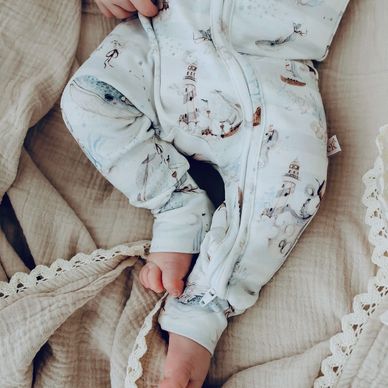 Baby in a light blue onesie with lighthouse prints, lying on a beige textured blanket.