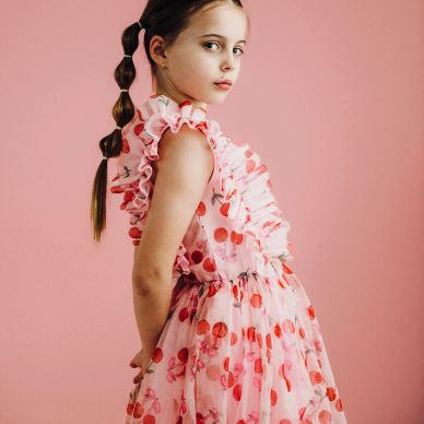 Young girl in a pink cherry-patterned dress against a pink background.