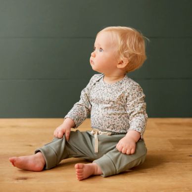 Blond baby sitting on wooden floor looking to the side.