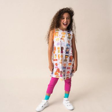Happy girl wearing colorful outfit and white sneakers, standing against a plain background.