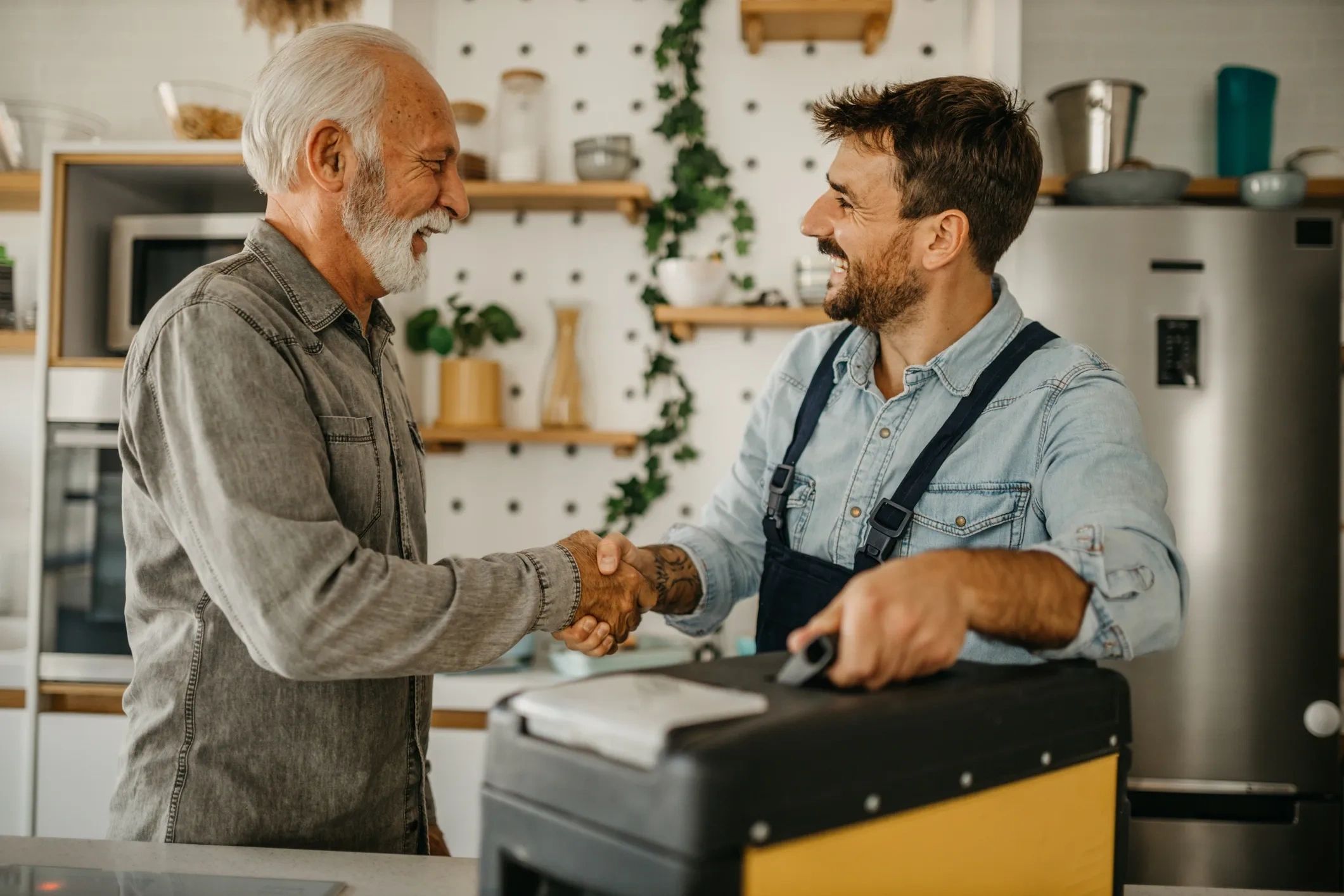 Older man shaking hands with a smiling handyman holding a toolbox.