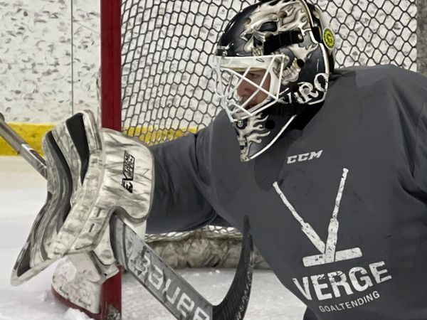 Hockey goalie making a save in front of the net on ice rink.