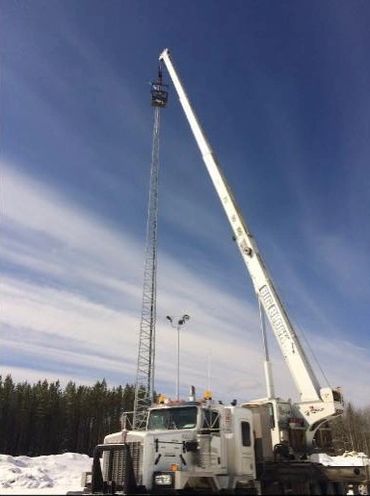 A crane lifting workers to the top of a tall communication tower in a snowy area.