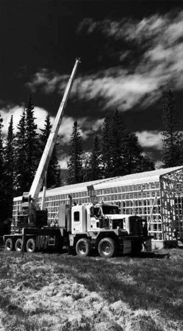 A crane truck at a construction site in a forested area under a cloudy sky.
