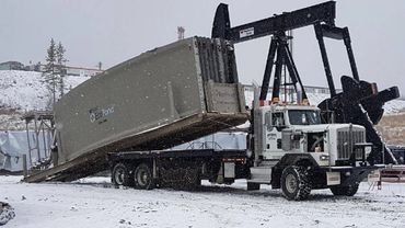Large white truck unloading an EcoPond container in a snowy oilfield.