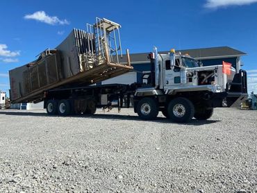 A semi truck with a tilted flatbed trailer on a gravel lot.