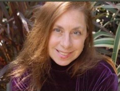 Smiling woman with long hair in a purple top outdoors.