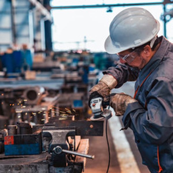 Worker using grinder on metal in industrial workshop.