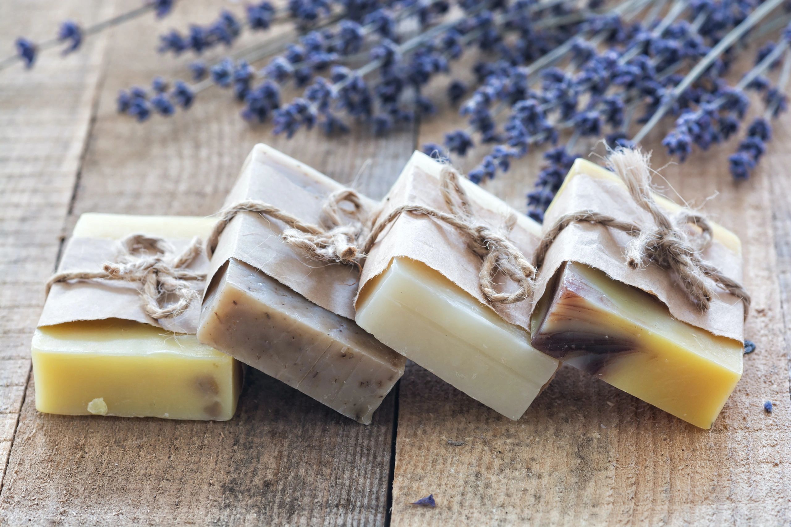 handcrafted soap bars with brown paper and twine. Lavender is in the background, hardwood floor
