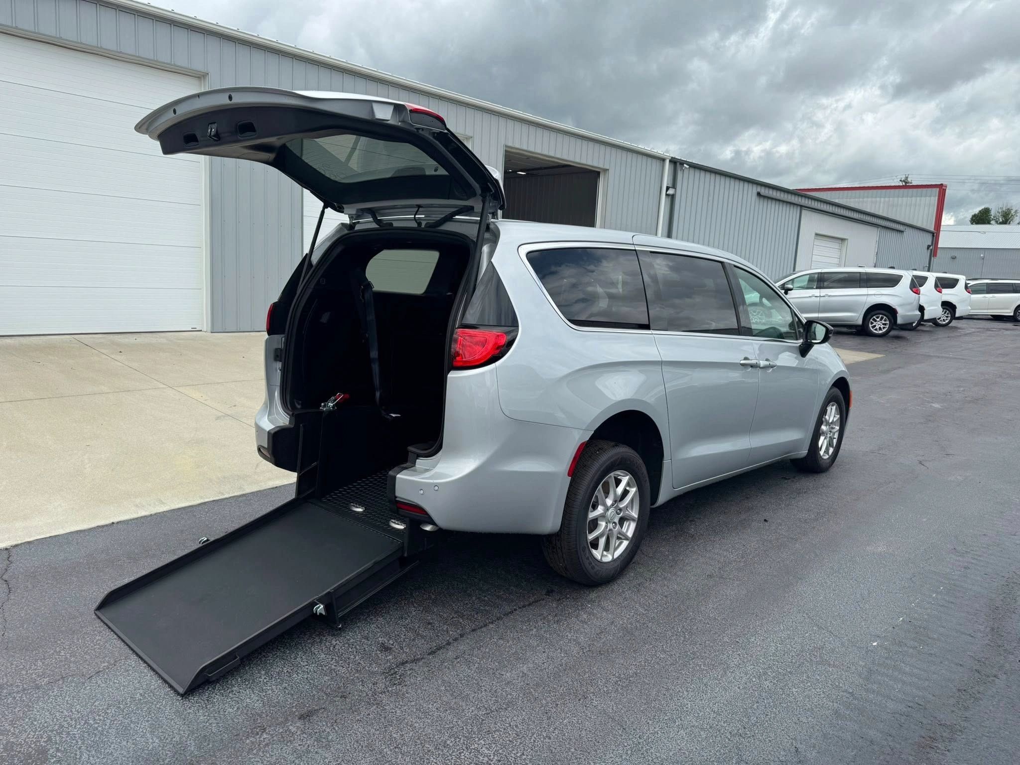 Silver wheelchair-accessible van with rear ramp deployed.