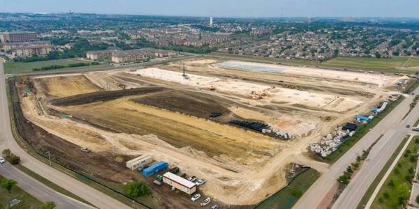 A large construction site with cleared land and construction vehicles near a suburban area.