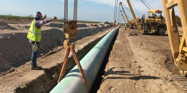 Workers installing a large pipeline in a trench at a construction site.