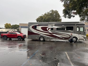 Red truck towing a large RV with a man walking beside it in a wet parking lot.