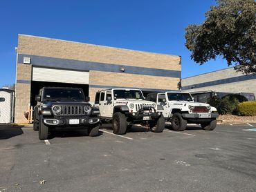 Three Jeep Wranglers parked outside a garage on a sunny day.