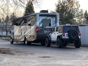 A Jeep towing a large RV on a quiet road.