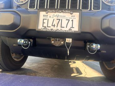 California license plate on a Jeep with tow hooks and electrical connector.