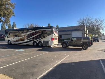 A Jeep towing a large, decorated RV in a parking lot on a sunny day.