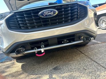 Close-up of a white Ford vehicle's front grille and tow hooks with a pink coiled cable.