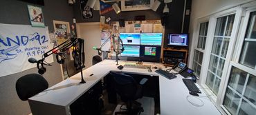 Radio broadcasting studio with microphones and multiple monitors.