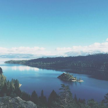 Tranquil lake surrounded by forest and mountains under a clear blue sky.