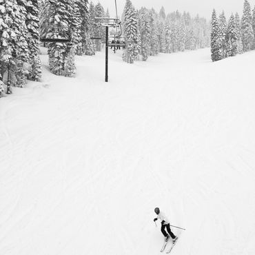 Skier descending a snowy slope surrounded by snow-covered trees and chairlifts.