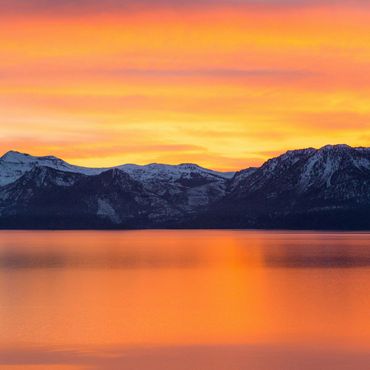 Snowy mountains reflected in a vibrant orange sunset lake.