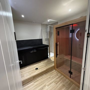 Modern sauna room with glass door and wooden floor.
