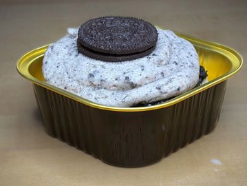Cookies and cream dessert topped with an Oreo cookie in a gold and brown container.