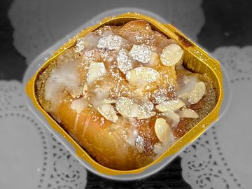 A sweet pastry topped with icing and almond slices in a yellow container.