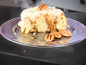 A slice of pecan cake with frosting on a glass plate.