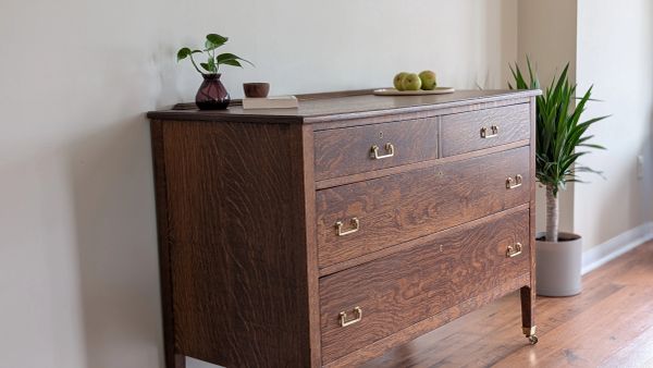 A wooden chest of drawers with brass handles in a bright room.