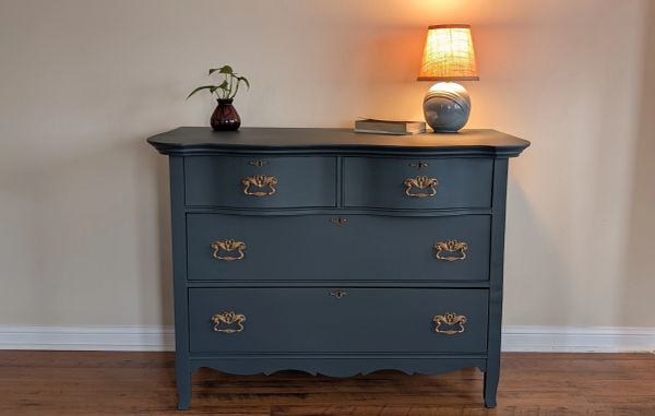 Blue vintage dresser with brass handles, topped with a lamp and small plant.