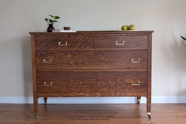 A vintage wooden dresser with brass handles in a minimalist room.