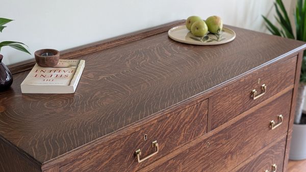 Wooden dresser with brass handles, decorated with a book, candle, and plate of pears.