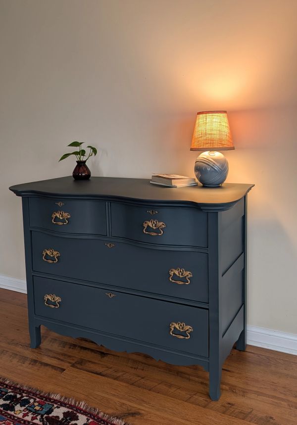 Blue vintage dresser with brass handles, decorated with a small lamp and plant.