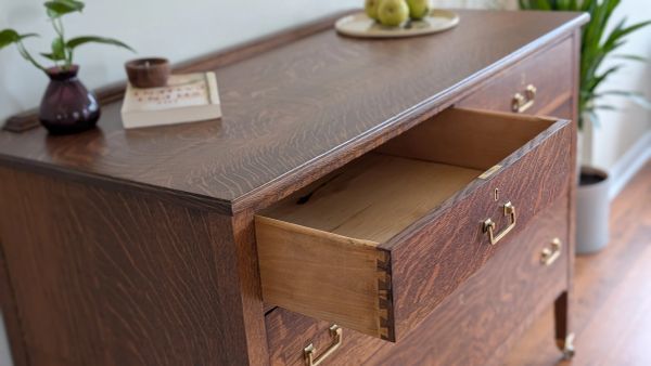 Wooden dresser with an open drawer and brass handles in a cozy room.