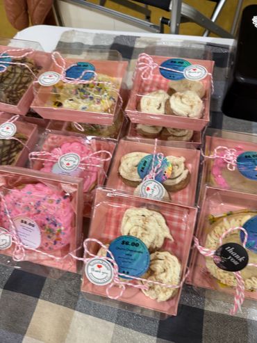 Assorted decorated cookies in clear pink boxes tied with twine on a checkered tablecloth.