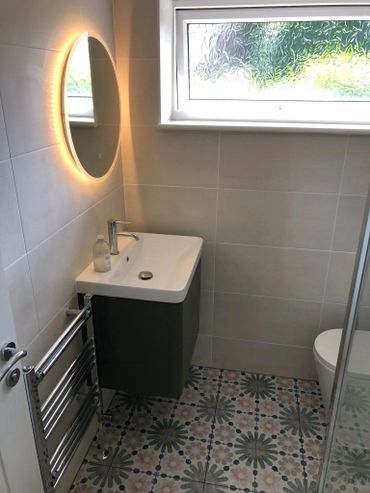 Modern small bathroom with patterned floor tiles and a glowing round mirror.