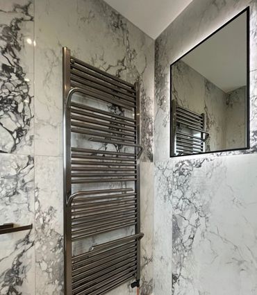Modern bathroom with marble walls and a sleek heated towel rack.