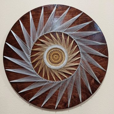 Intricate circular string art with white and brown threads on a wooden base.